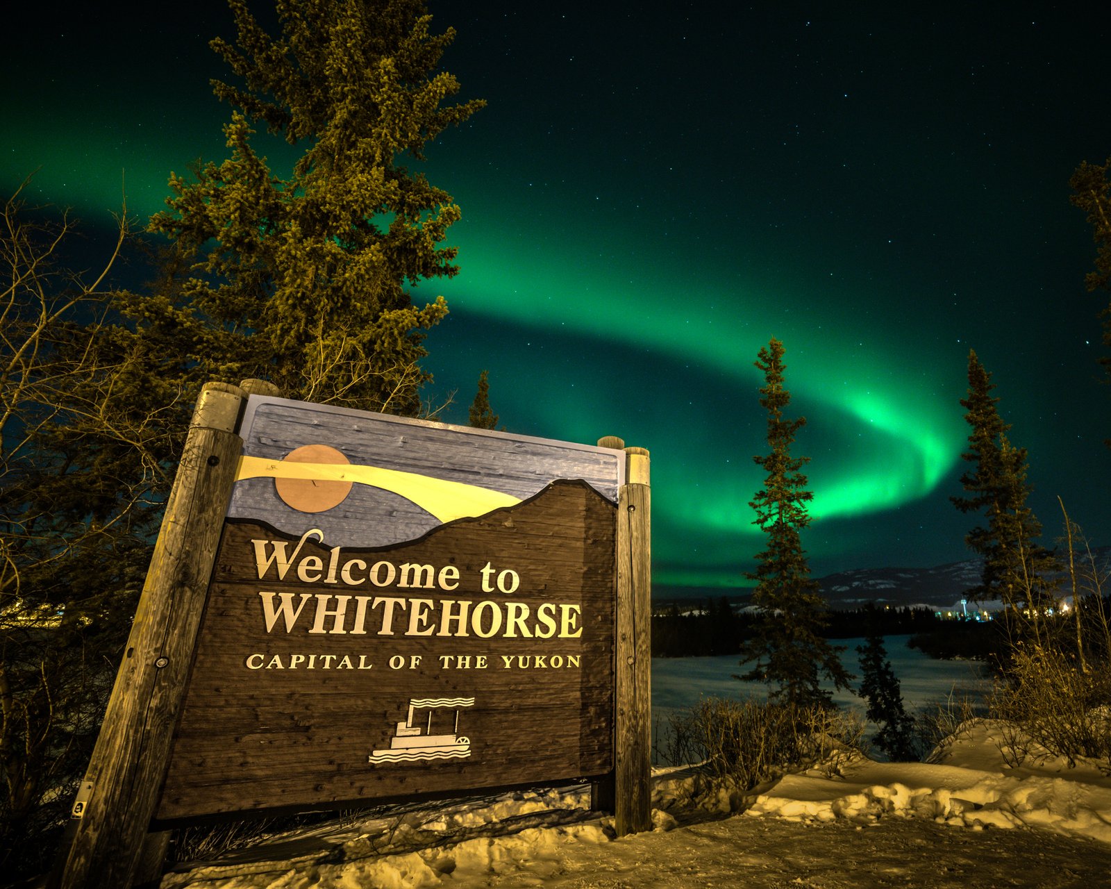 Welcome to Whitehorse sign in Yukon Territory with bright green aurora borealis northern lights wilderness city of arctic area.